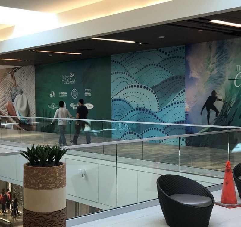 Mall interior with two people walking past a wall with ocean-themed promotional graphics.