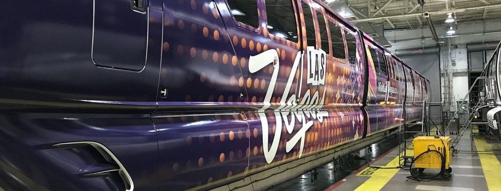 A Virgin train in a repair shop with purple and orange graphics.
