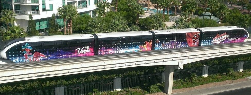 Monorail train in Las Vegas, decorated with colorful advertisements, travels along an elevated track.