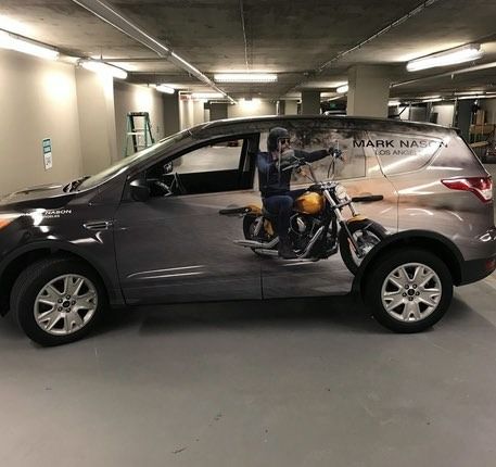 SUV with motorcycle image wrap in a parking garage; rider on the side.