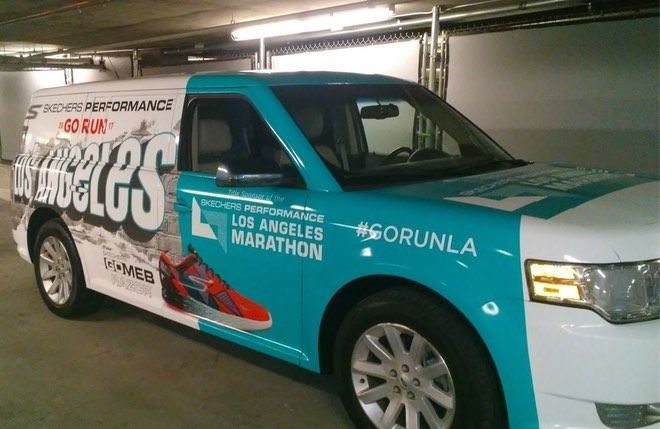 A van wrapped in turquoise and white advertising the Los Angeles Marathon; it has running shoe art.