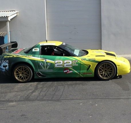 Green and yellow race car with the number 22, parked outside a building.
