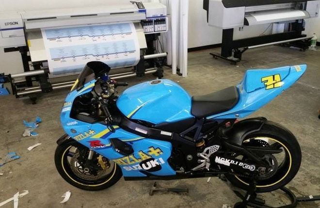 Light blue Suzuki sport motorcycle in a shop with large format printers.