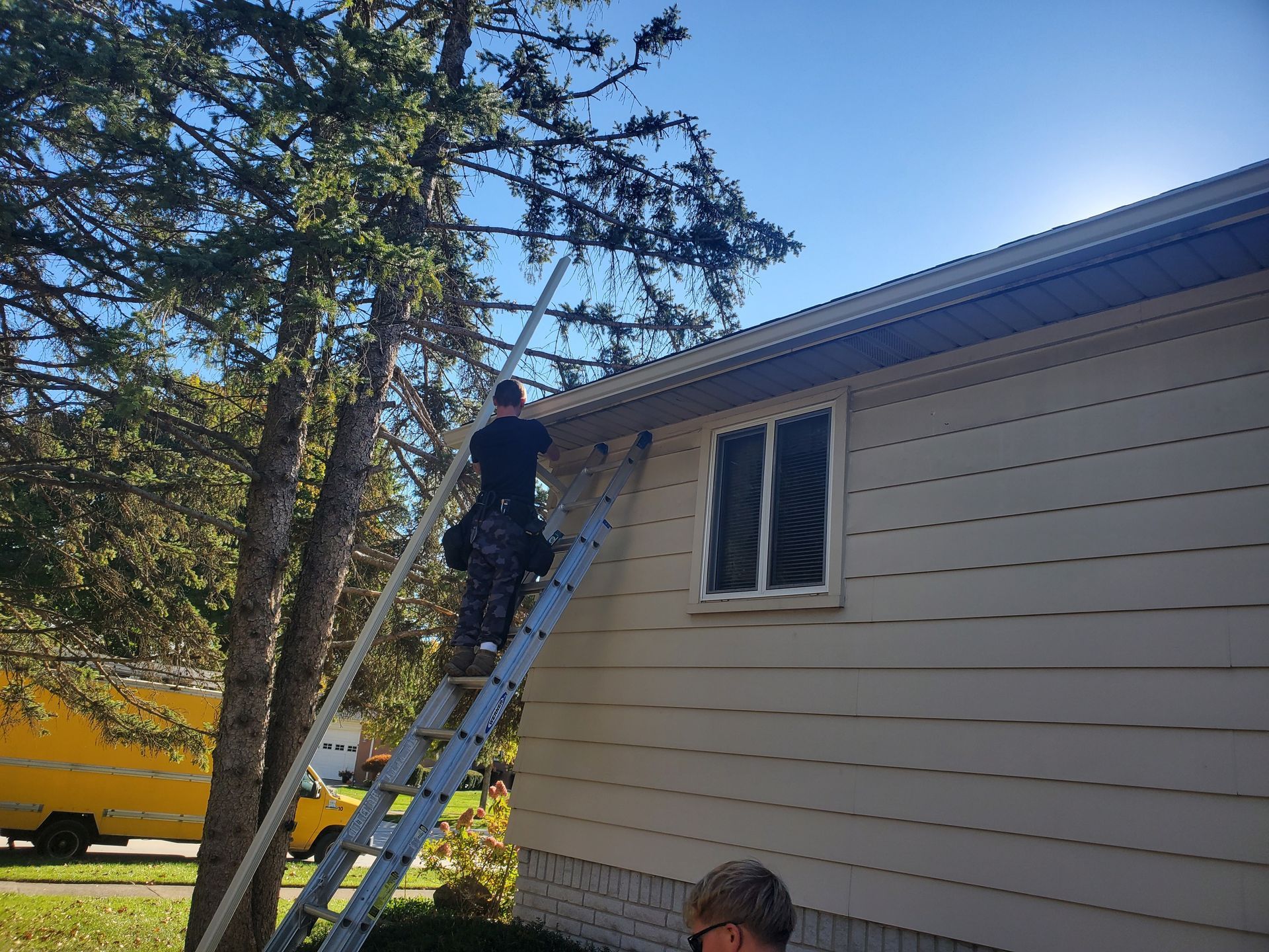 A man is standing on a ladder working on a gutter.