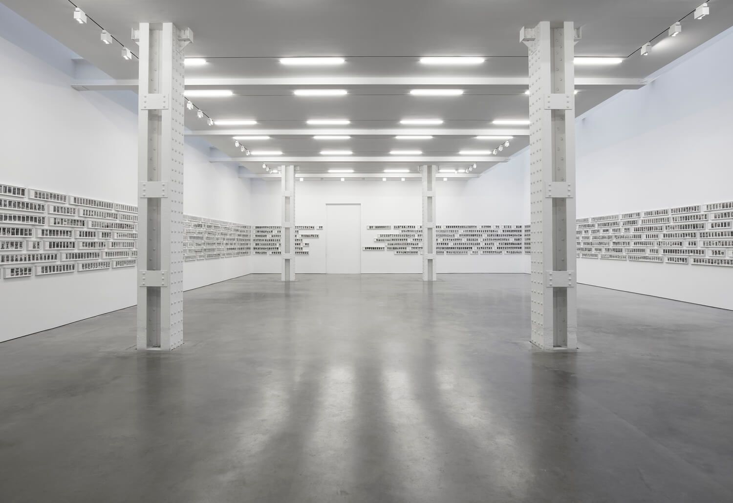 White art gallery with concrete pillars and photographs mounted on walls.