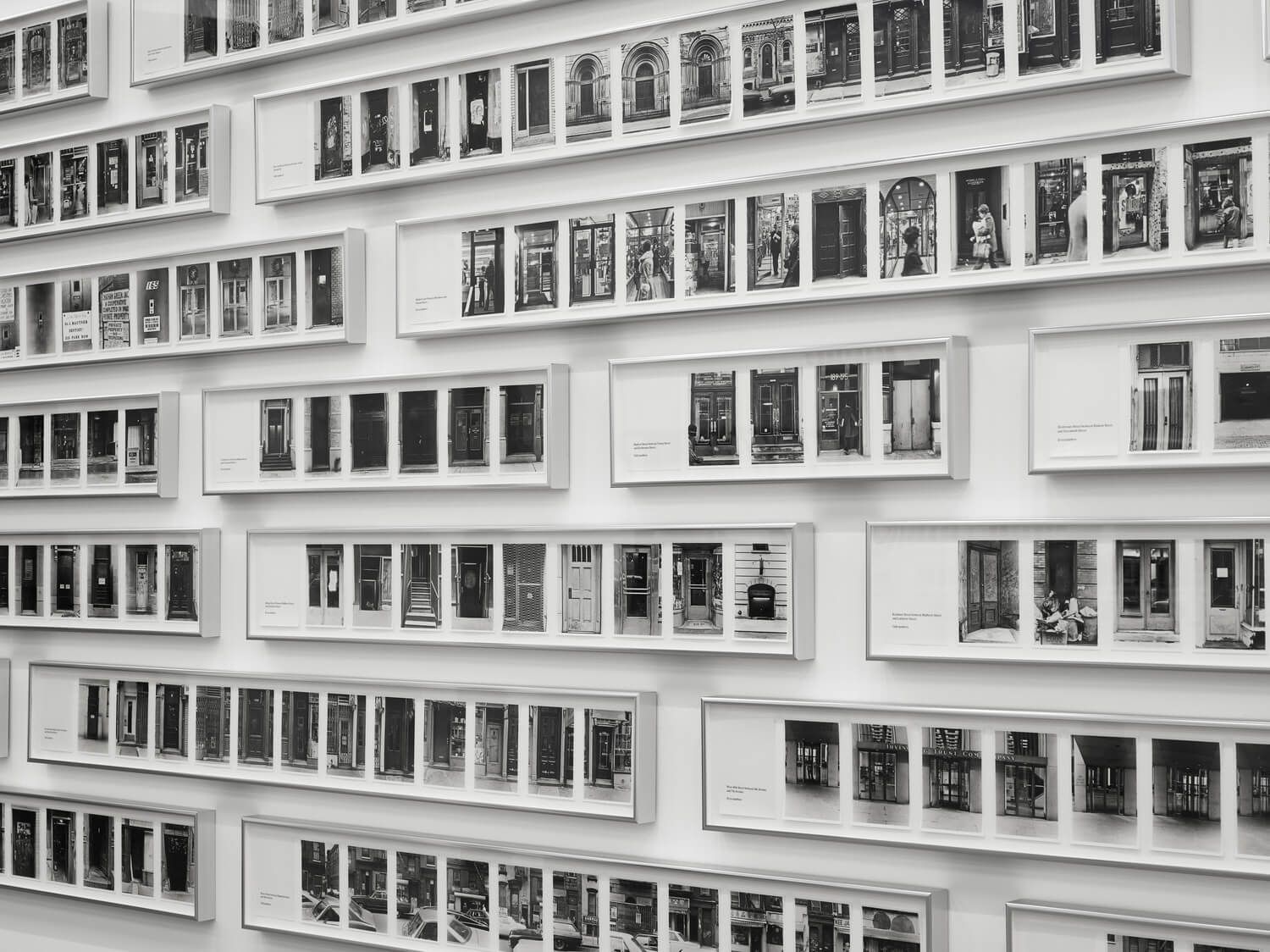 Rows of framed black and white photos of doors displayed on a white wall.
