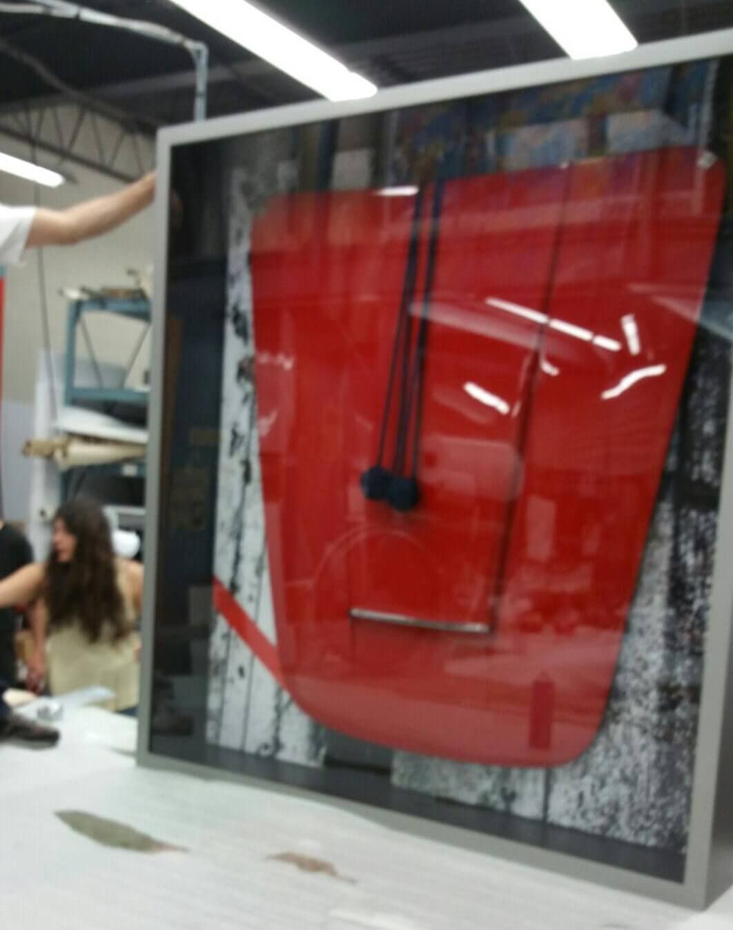Large red abstract art piece in a frame, on a table. Two people in the background.