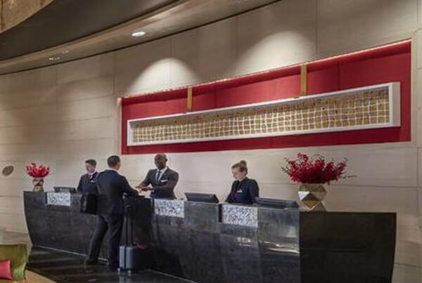 Hotel reception desk with employees assisting guests. Red accent wall.