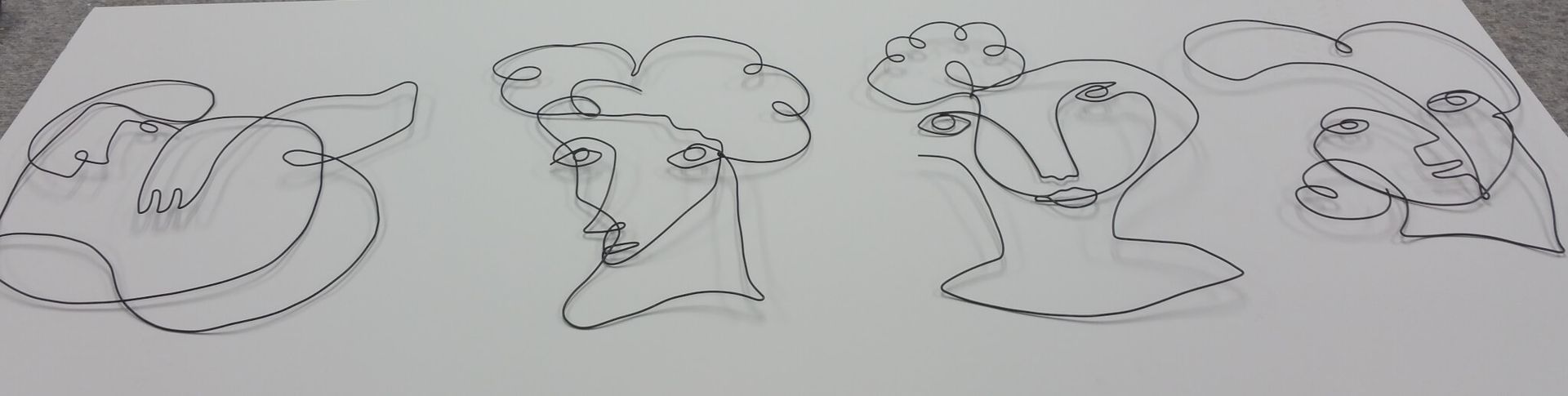 Four wire sculptures of faces on a white surface.