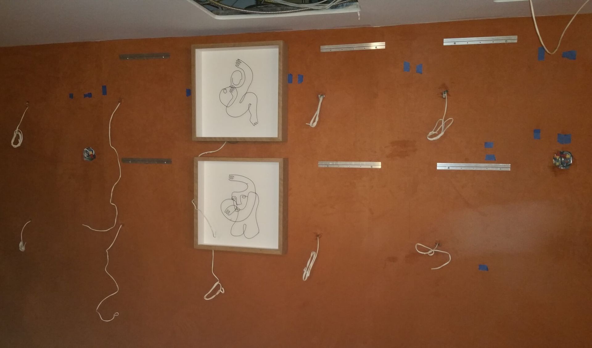 Orange wall with two framed drawings, metal strips, and wiring attached with tape.