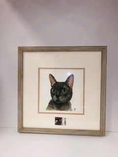 Framed watercolor painting of a black cat with yellow eyes; tan frame with white matting.