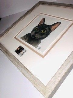 Framed watercolor painting of a black cat with yellow eyes; light gray frame, tan matting.