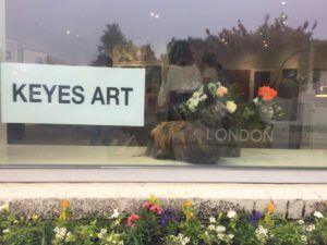 Keyes Art gallery storefront with floral display, London. White sign, glass window, and colorful flowers below.