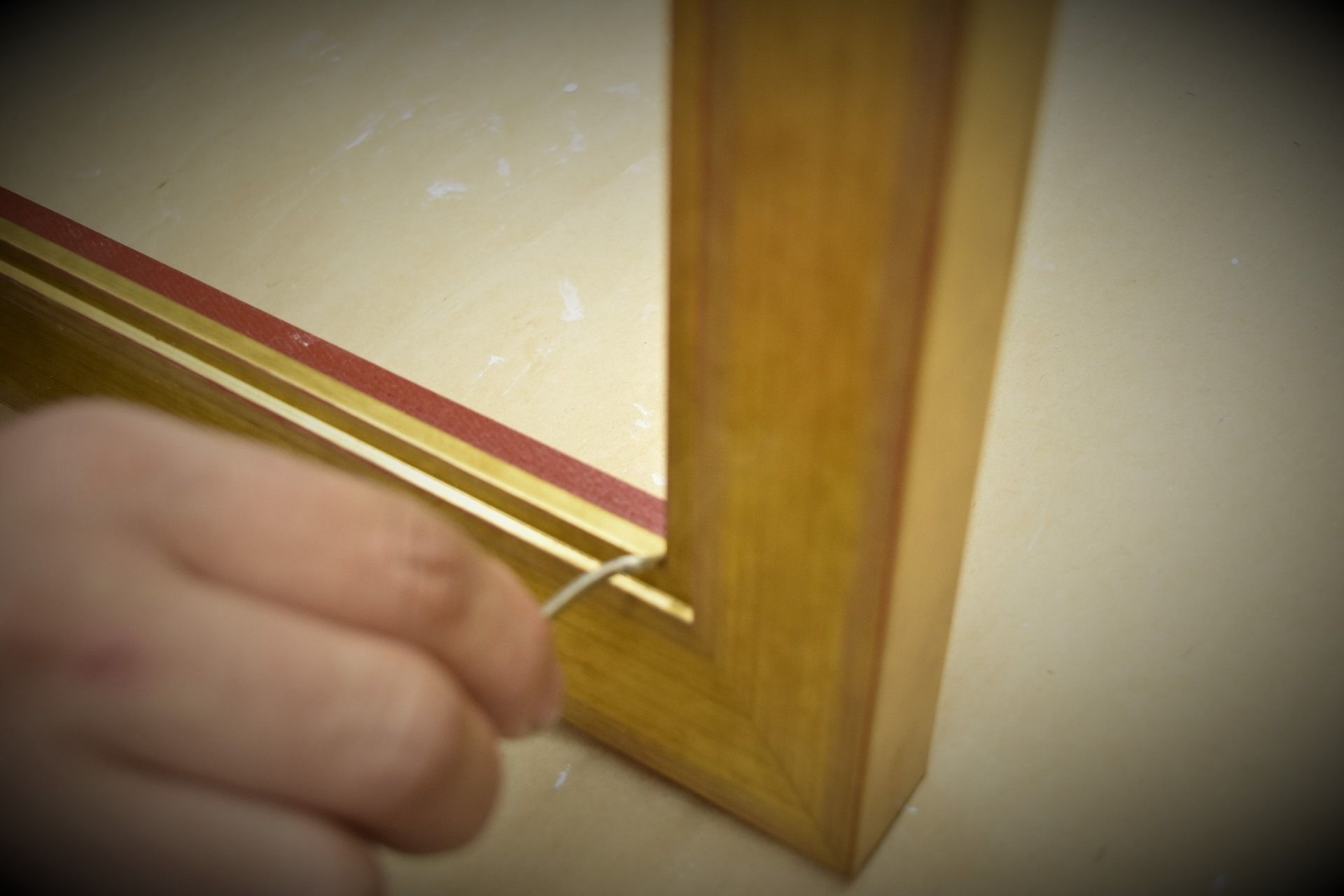 Hand inserting wire into a wooden picture frame, close-up view.