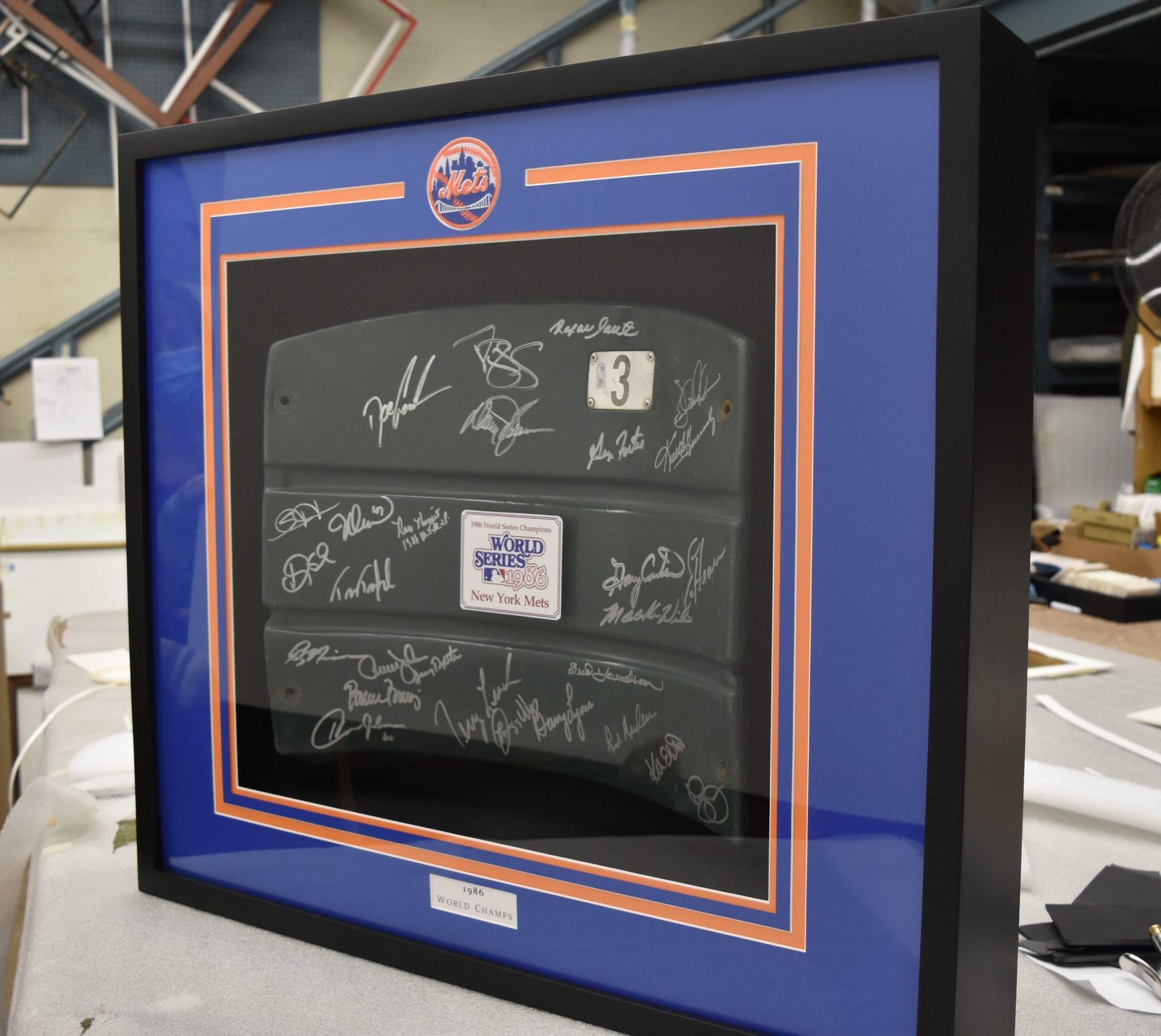 Framed baseball memorabilia featuring autographs on a gray object, surrounded by blue and bronze matting, in a black frame.