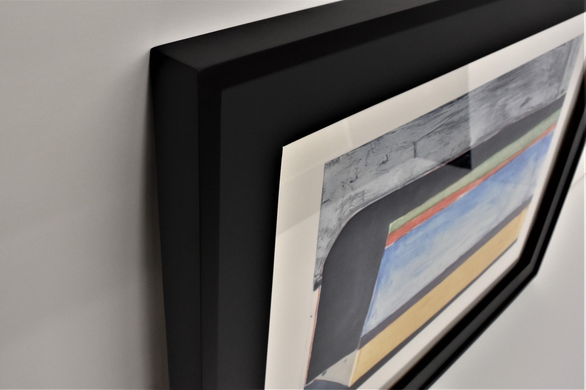 Black framed artwork on a white wall; abstract painting with blues, grays, and yellows.