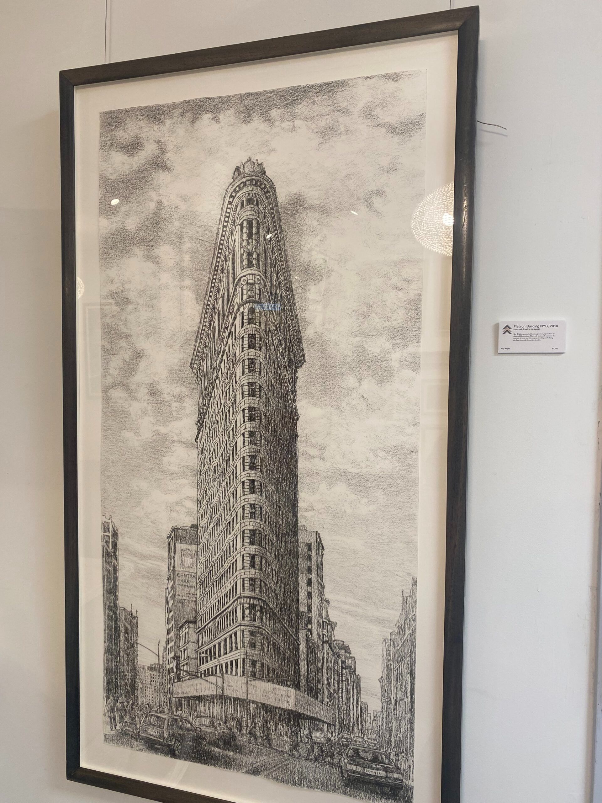 Black and white artwork of a skyscraper and cityscape, framed and mounted on a white wall.