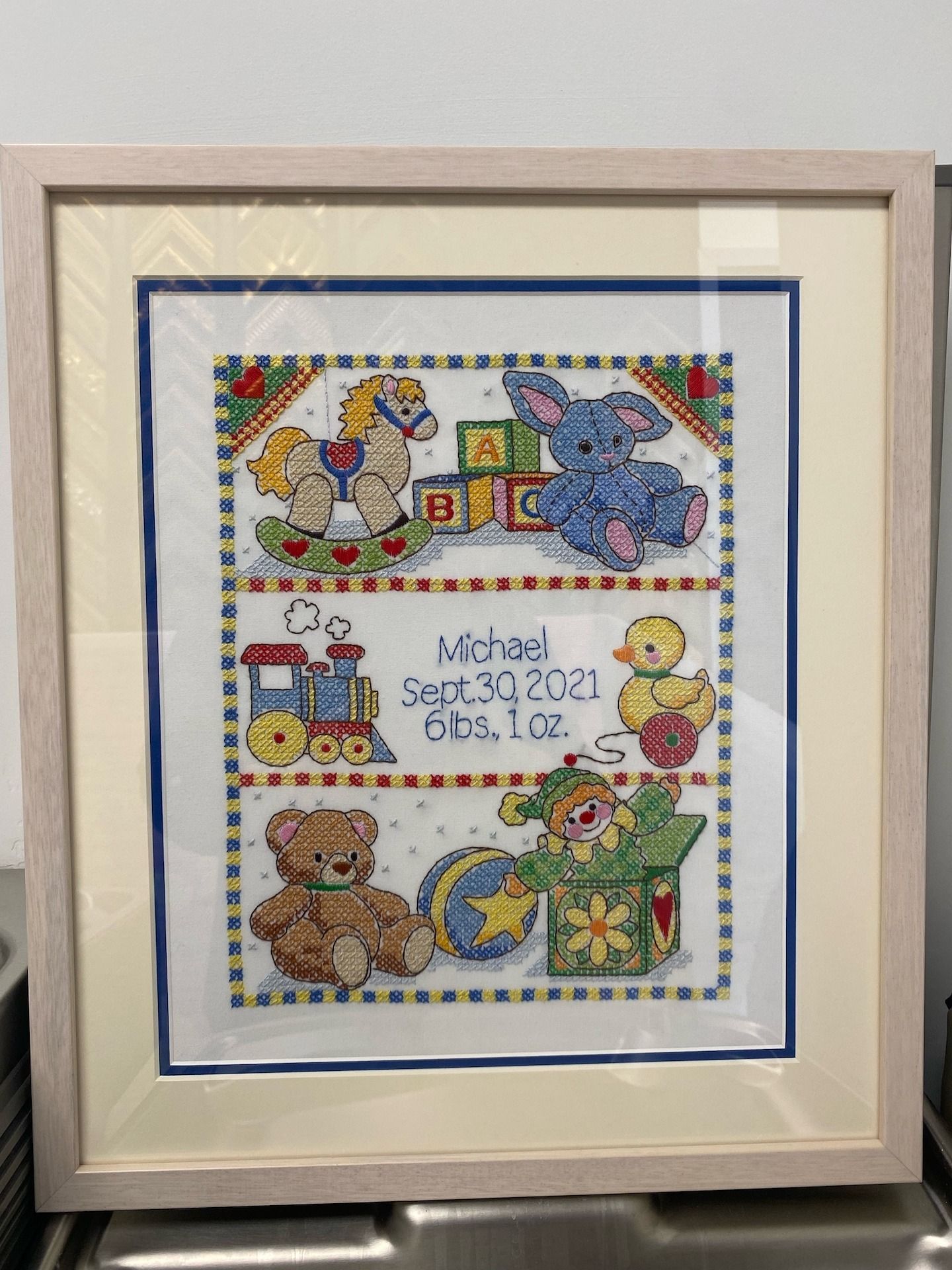 Cross-stitch baby announcement framed with toys and birth details: Michael, September 30, 2021, and weight.