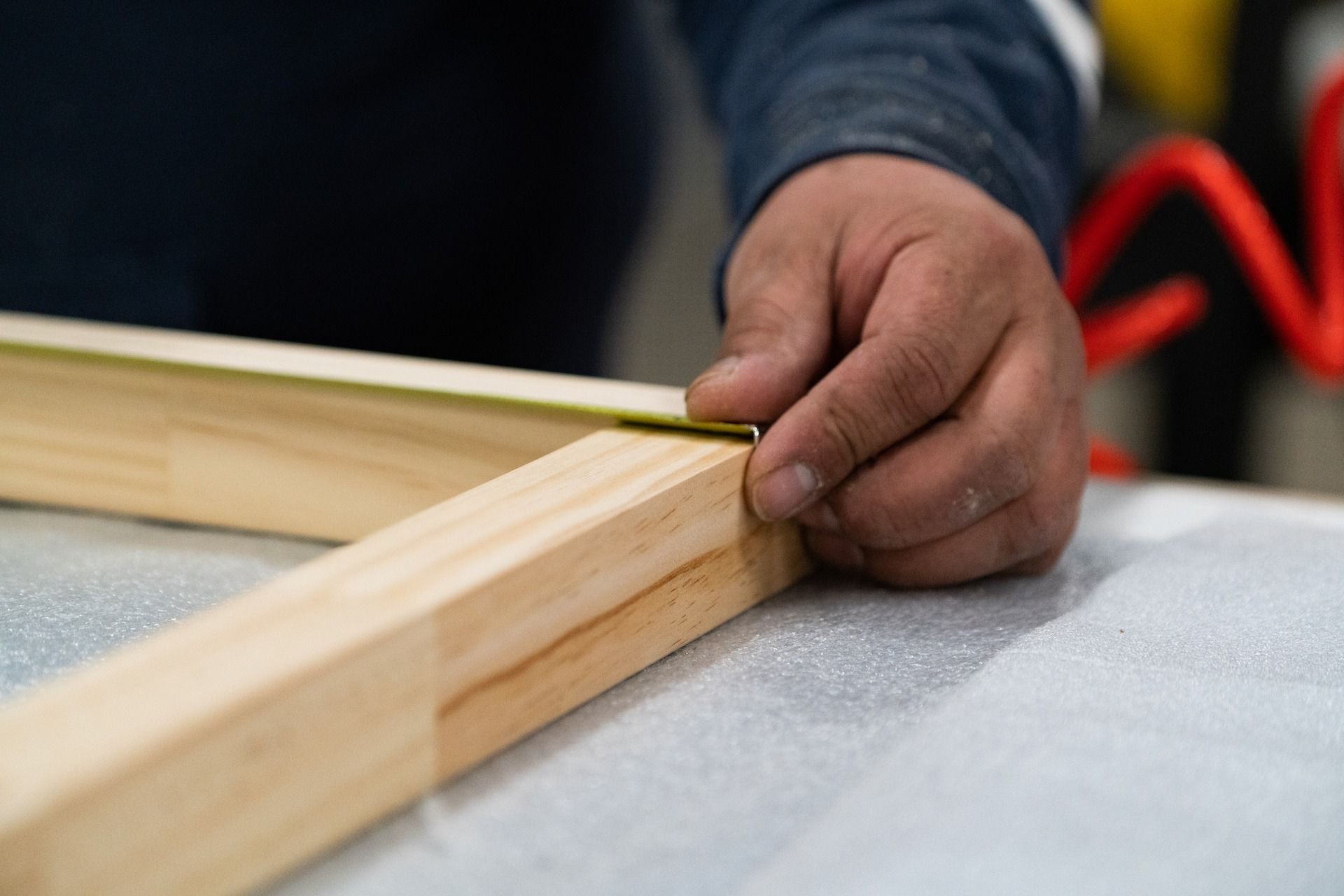 Person measuring wooden frame with a measuring tape on a table.