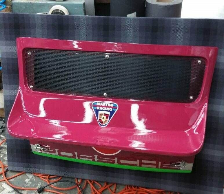 A pink Porsche rear engine lid with Martini Racing logo, black grill, and green trim.