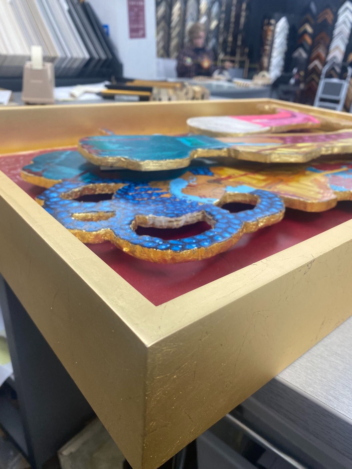 Gold framed artwork with colorful coasters layered on a red background.