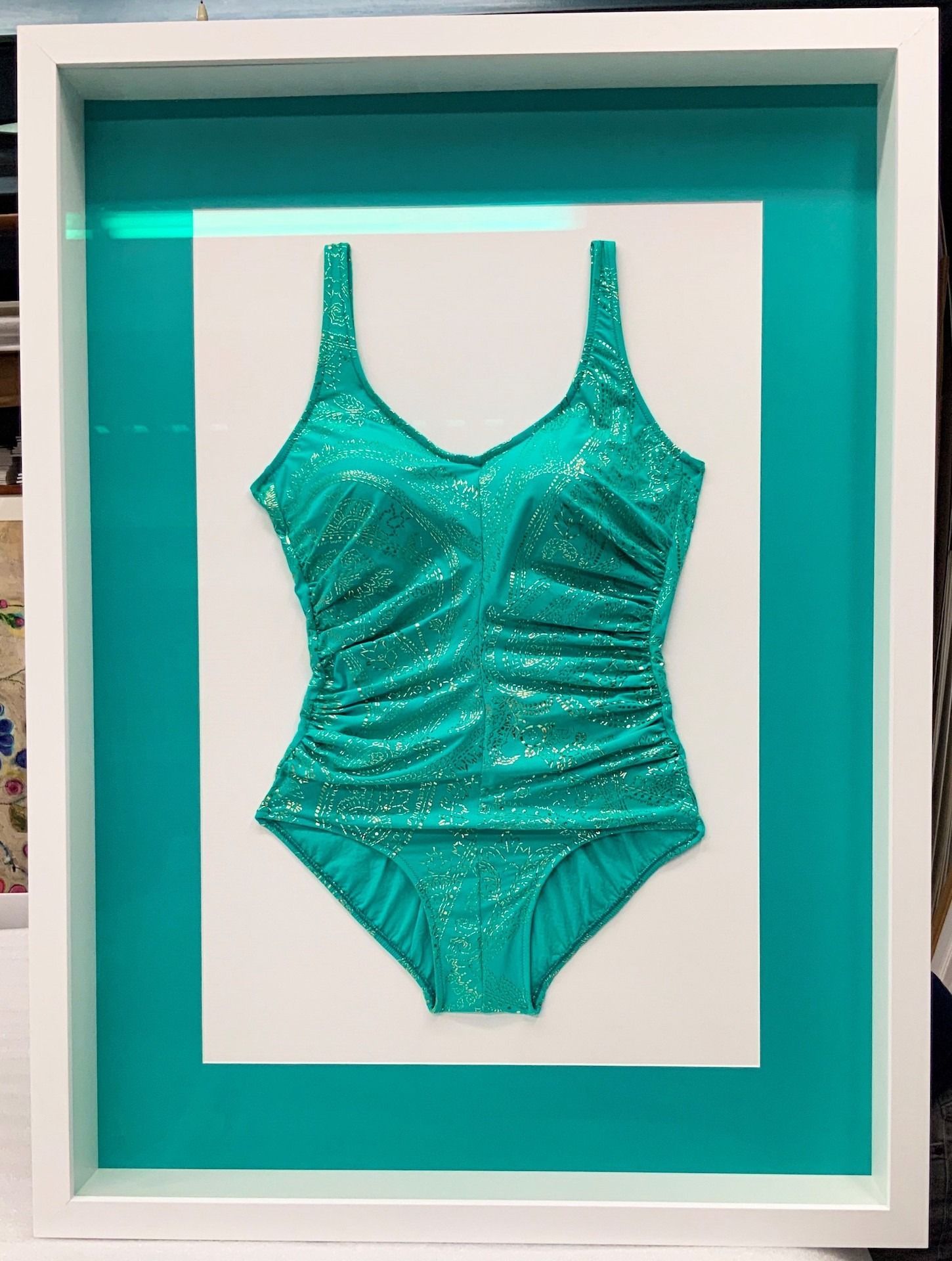 A teal, sparkly swimsuit framed in white, set against a teal background.