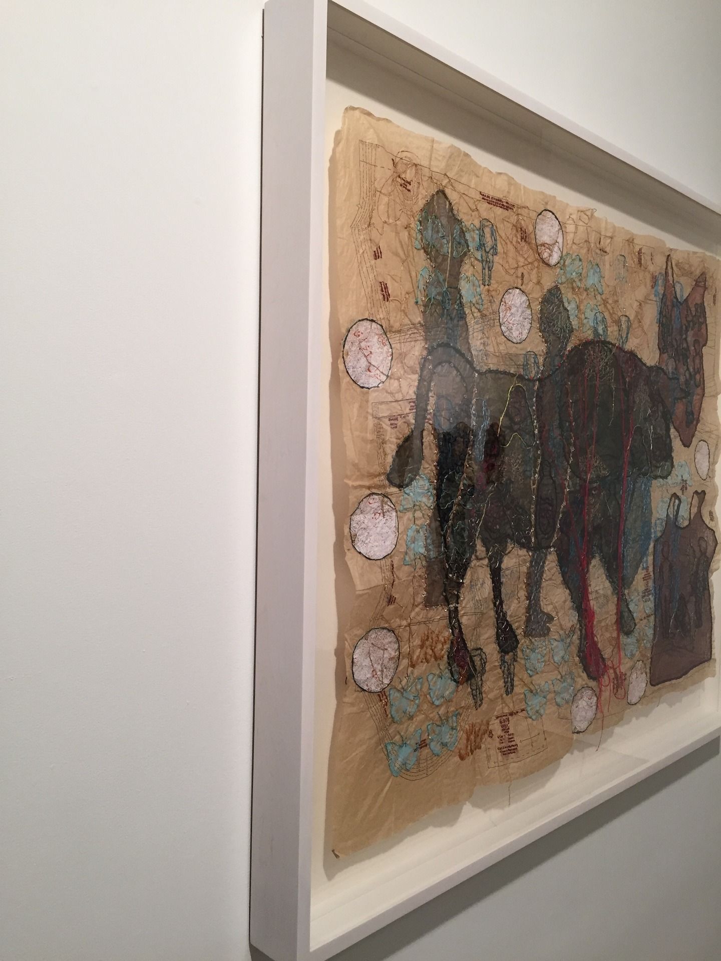 Artwork of horses with abstract shapes, framed in white, against a white wall.