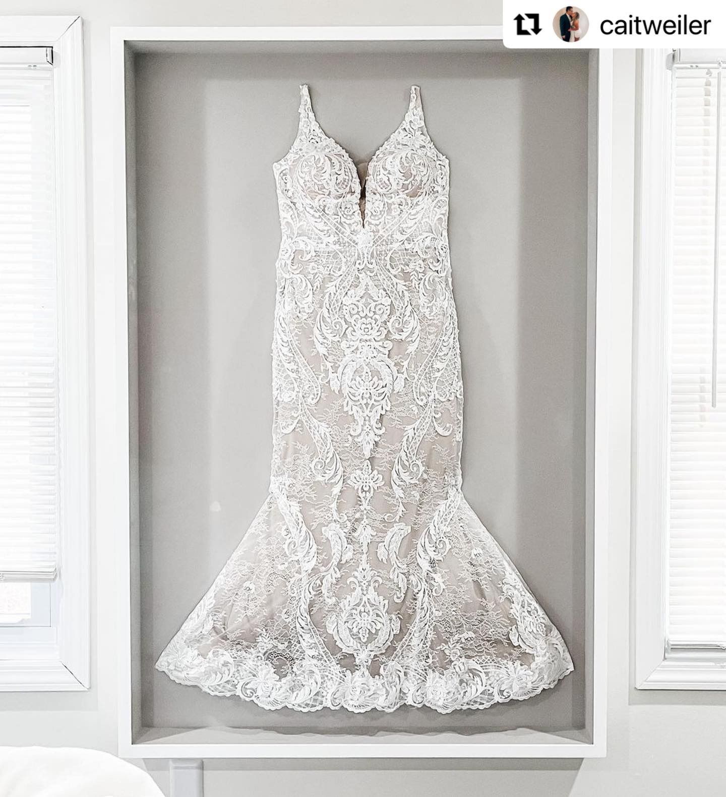 White lace wedding dress framed on a gray wall.