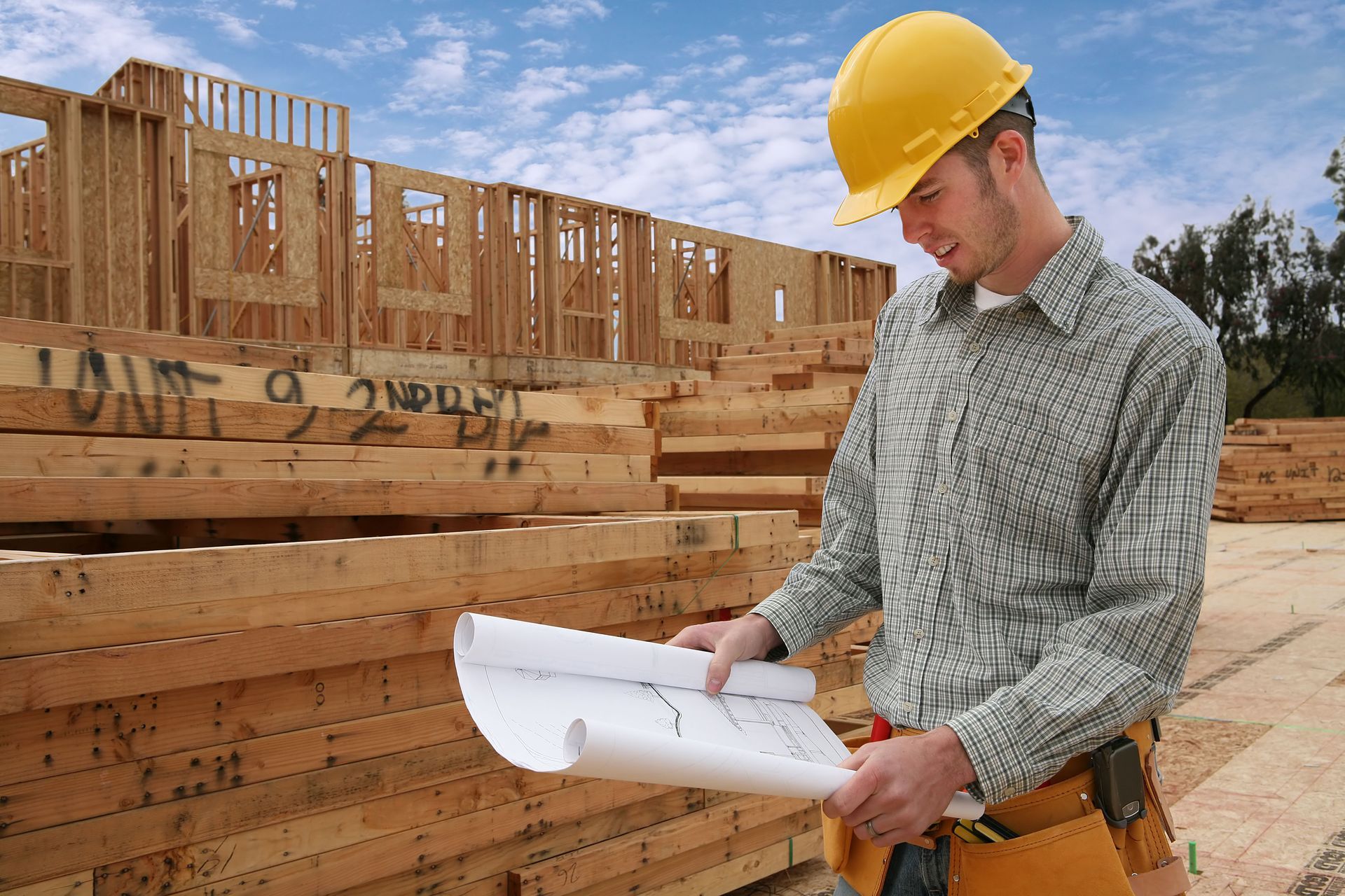 Construction worker in a yellow hard hat reviewing blueprints at a building site.