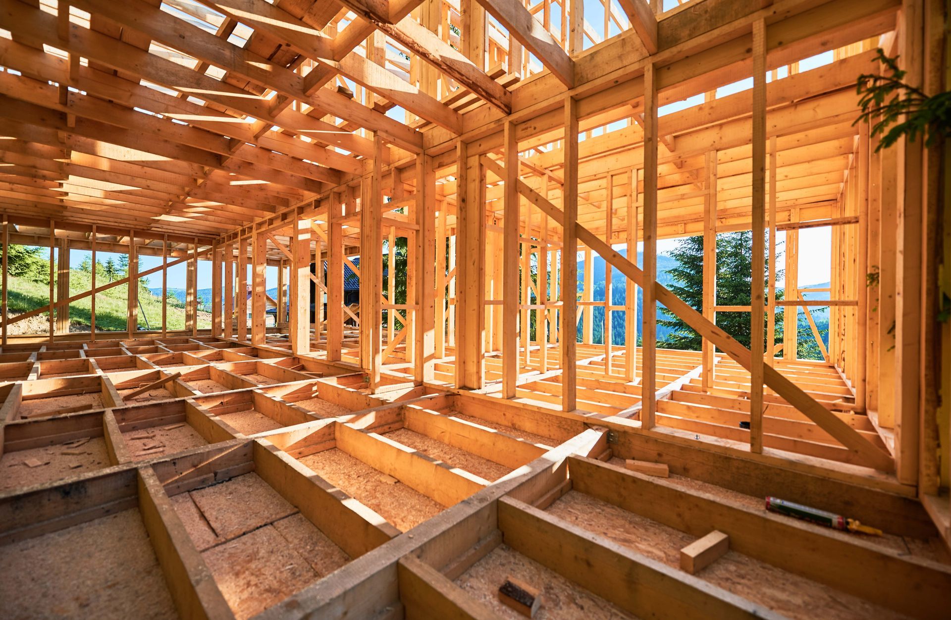 Sunlit wooden house frame under construction with exposed beams and floor joists.