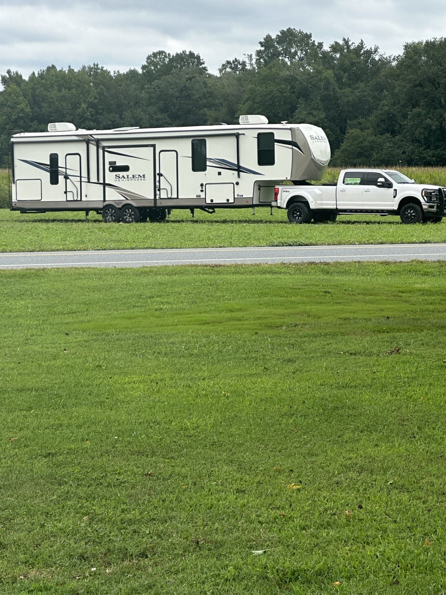 a white truck is towing a trailer in a grassy field.