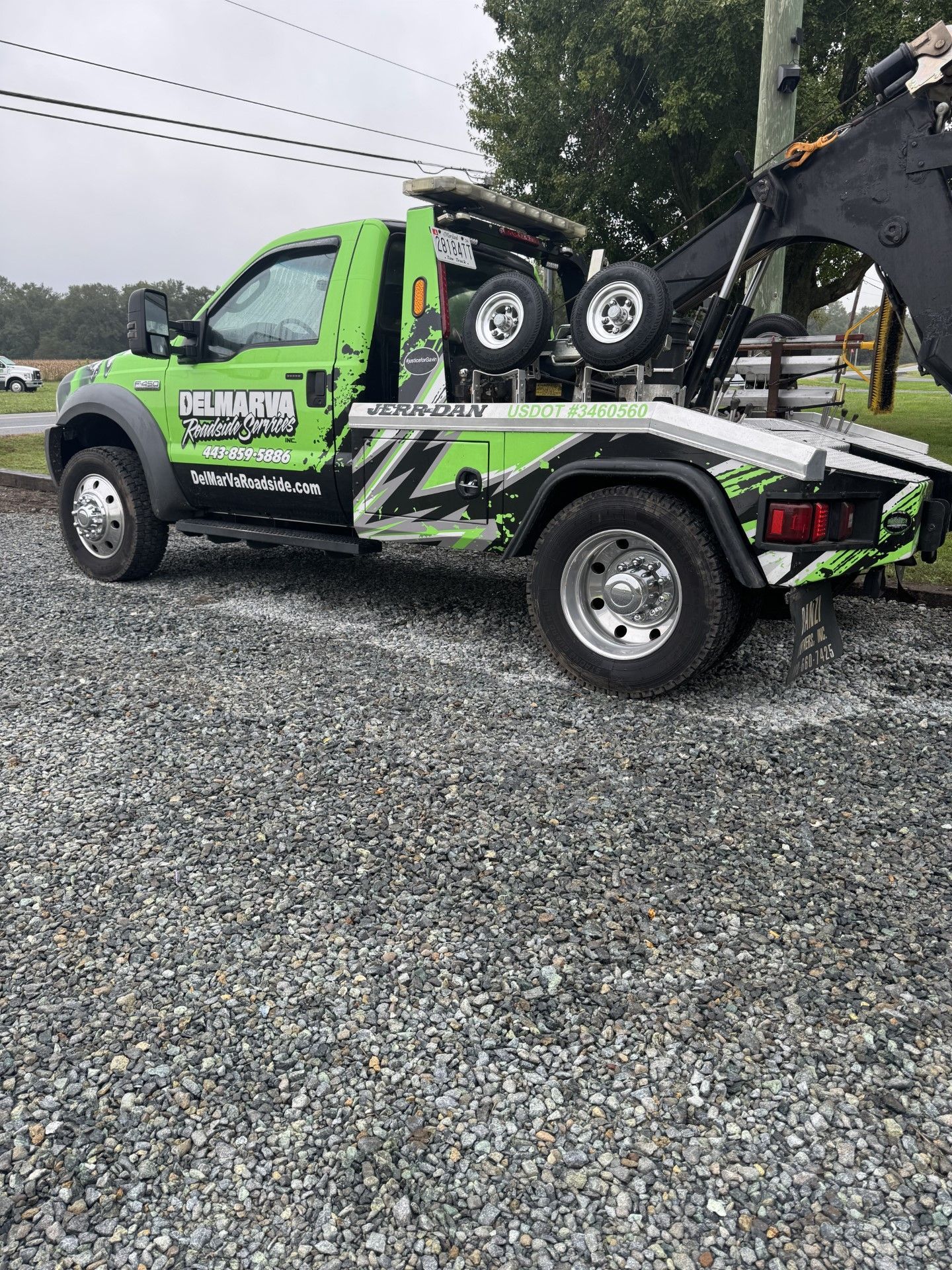 a green tow truck is parked in a gravel lot.