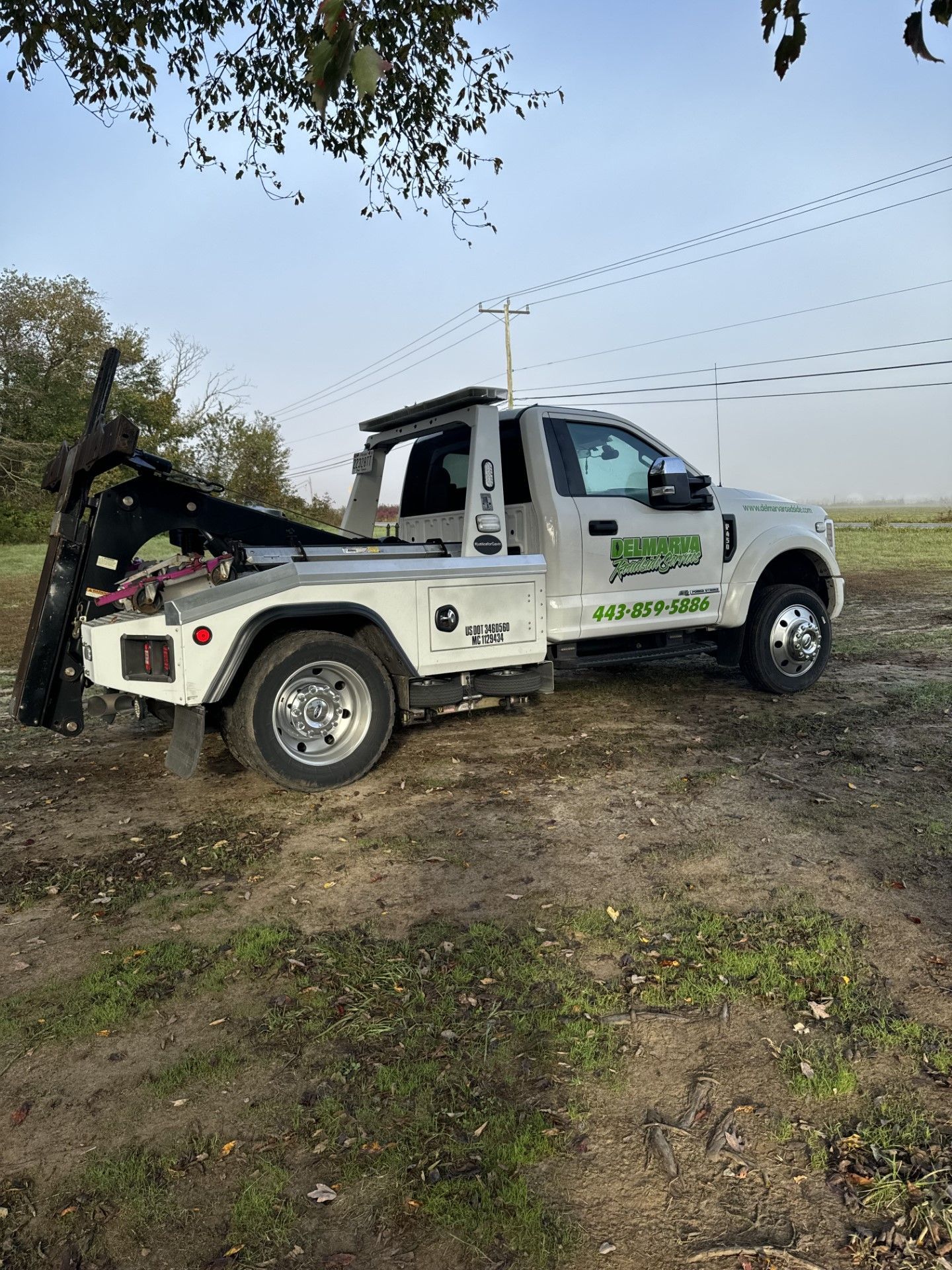 a white tow truck is parked in a dirt field.