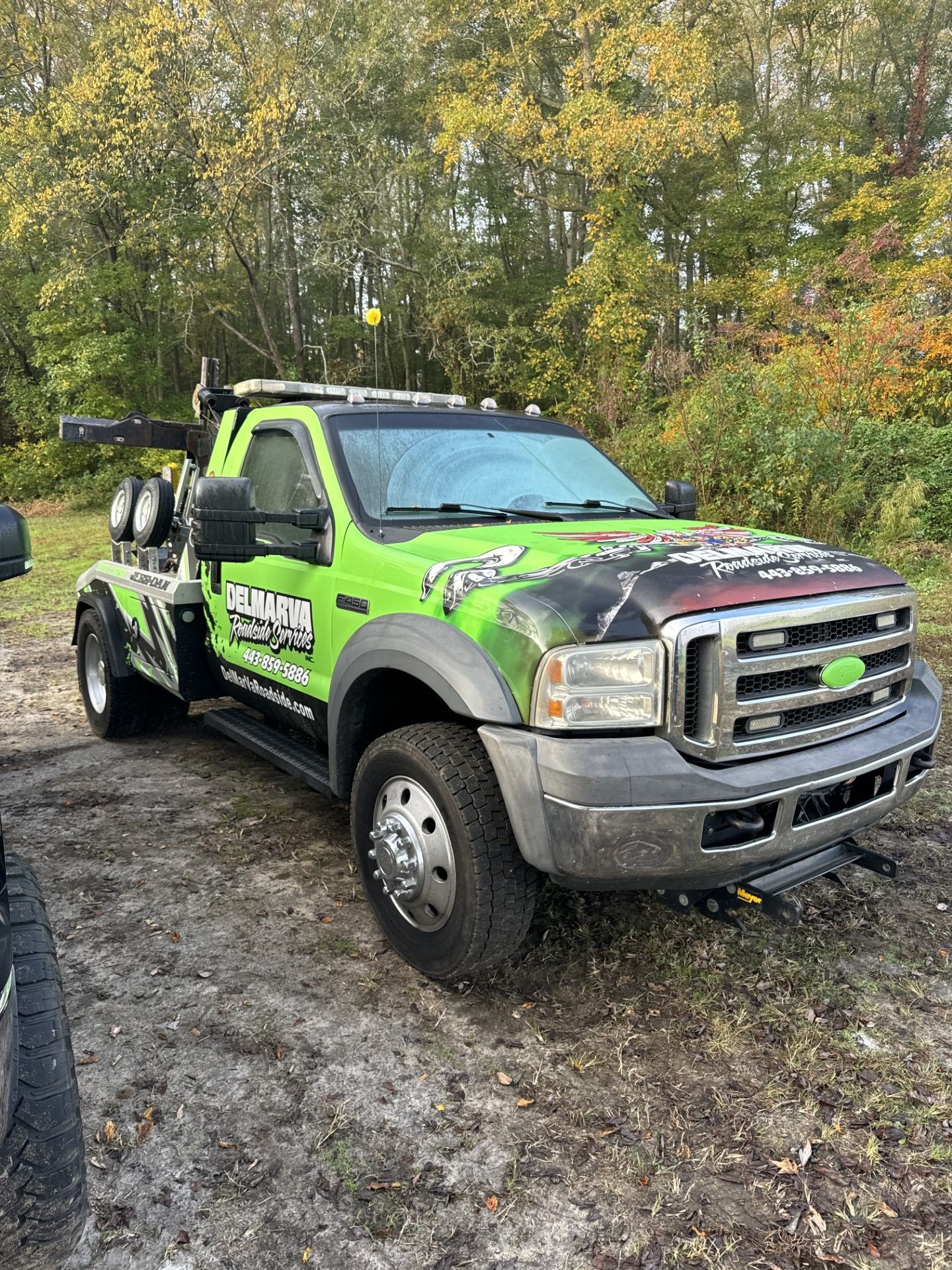 a green tow truck is parked in a dirt field.