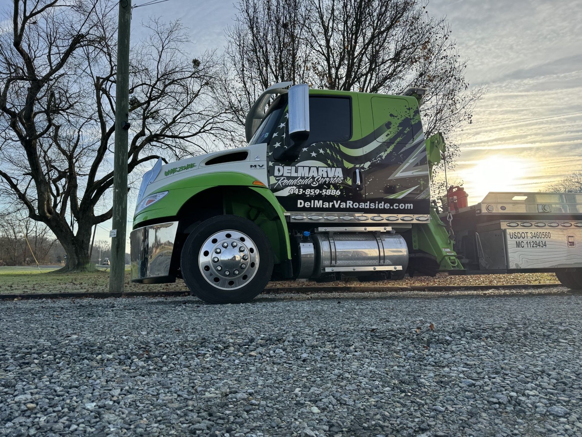 a green and white tow truck is parked on a gravel road.