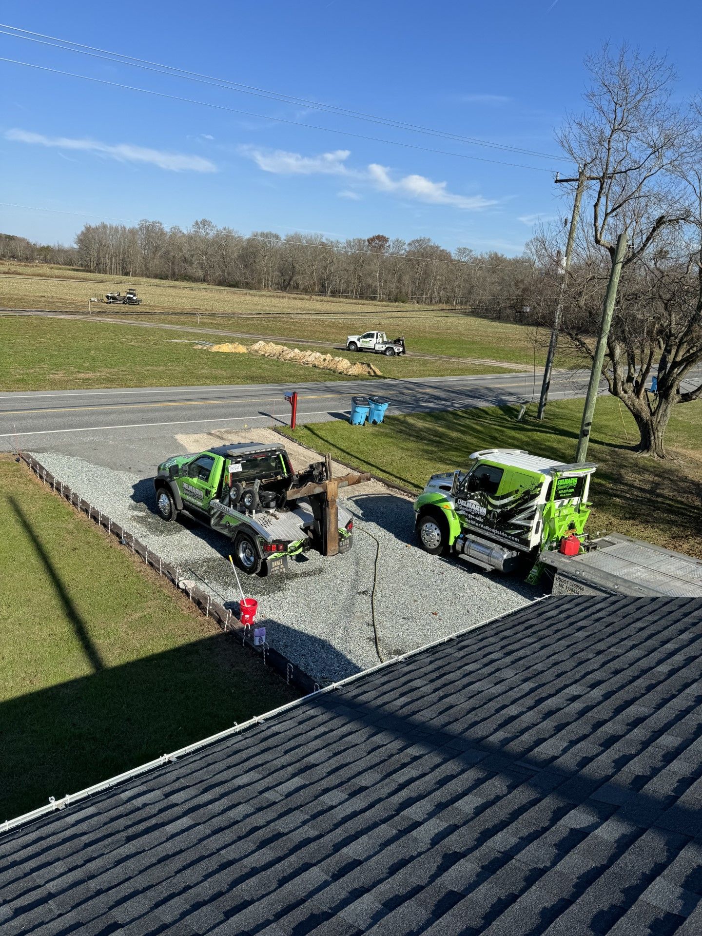 two green trucks are parked on the side of the road next to a house.
