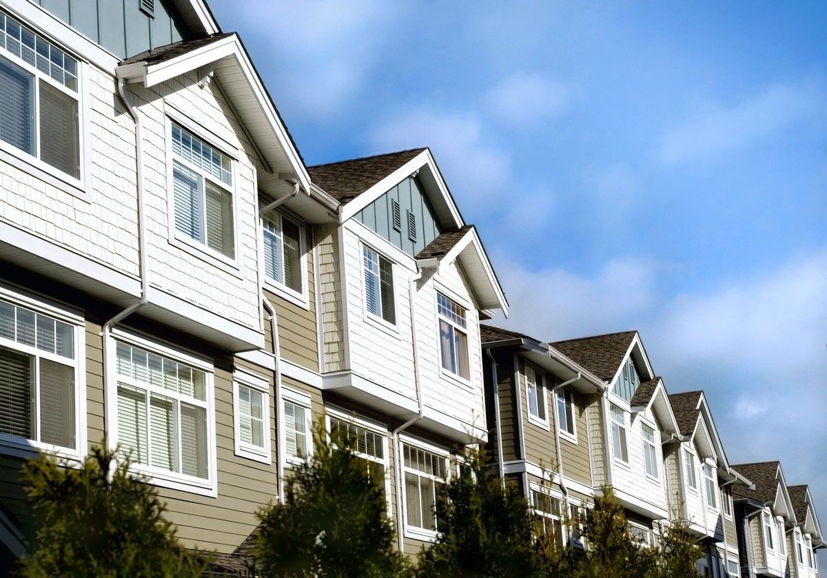 Row of townhouses with white trim, beige siding, and blue sky.