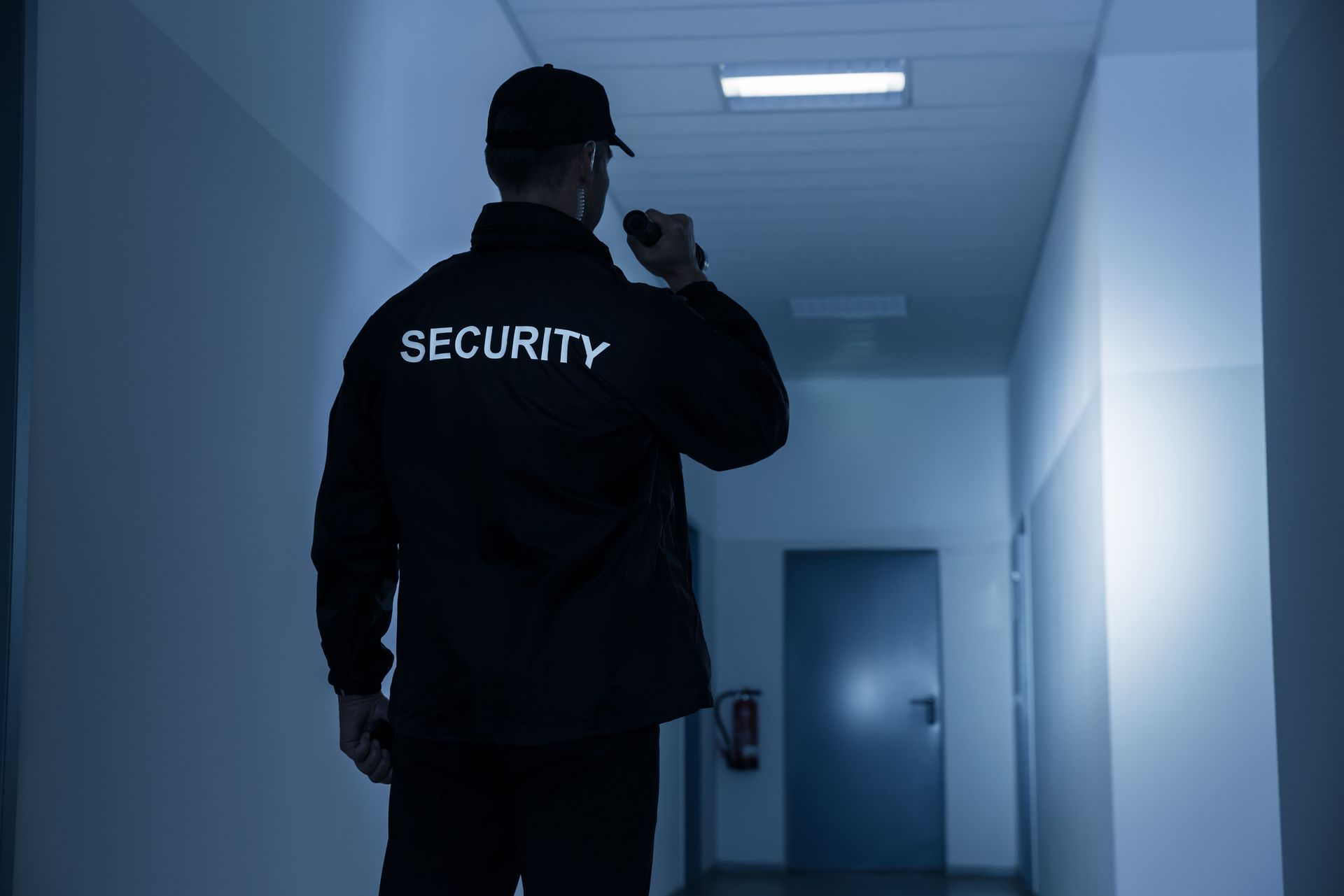 Security guard walks down a hallway, holding a radio, wearing a uniform that reads "SECURITY."