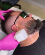 Person with black sunglasses lying back while another person applies a white facial mask.