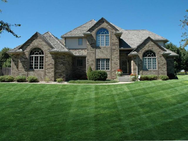 Two-story brick house with a manicured lawn under a clear blue sky.