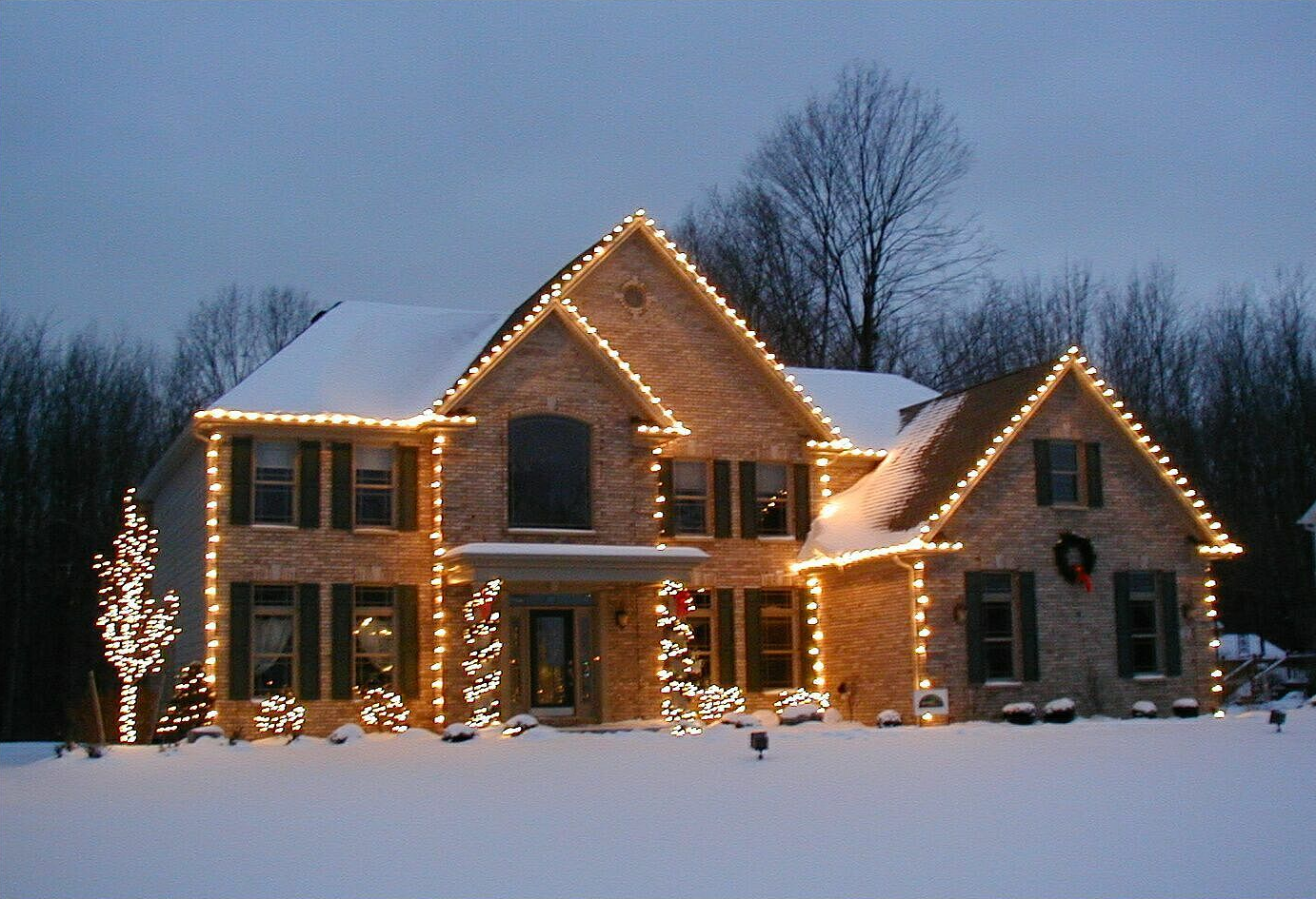 House with Christmas lights and snow-covered roof; winter evening.