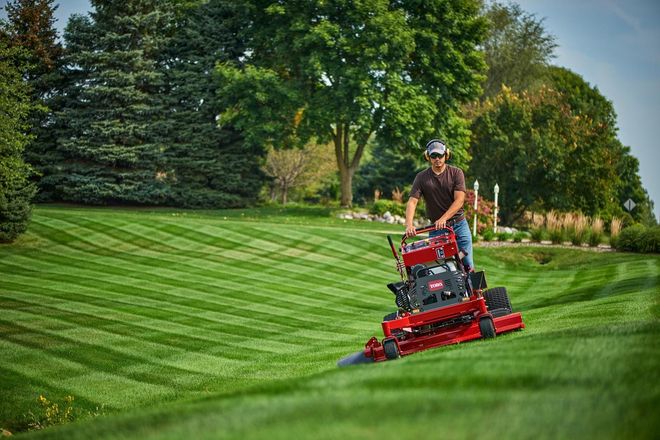 Man mowing grass with a red zero-turn mower on a sloped lawn.