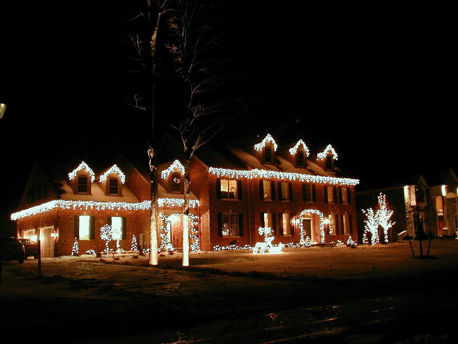 Large brick house at night, lit up with Christmas lights, snow on roof.