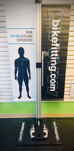 A man is standing in front of a sign that says bikefitting.com.