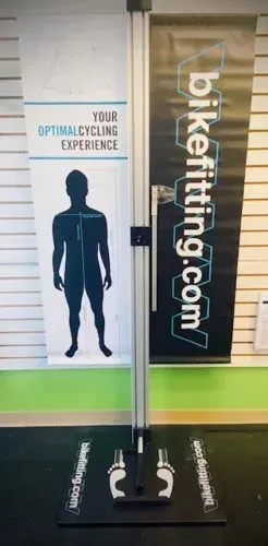 A man is standing in front of a sign that says bikefitting.com.