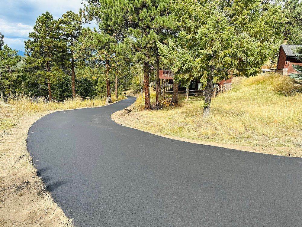 a curvy road going through a forest with a house in the background.