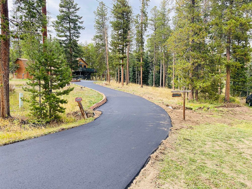 a curvy road going through a forest with a house in the background.