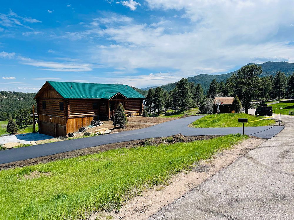 a log cabin with a green roof is sitting on top of a grassy hill next to a road.