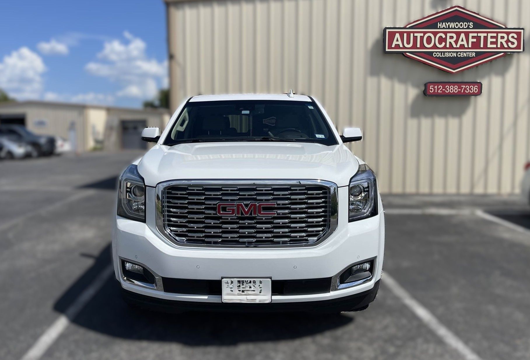 White GMC Yukon SUV parked in front of Autocrafters building, with a blue sky.