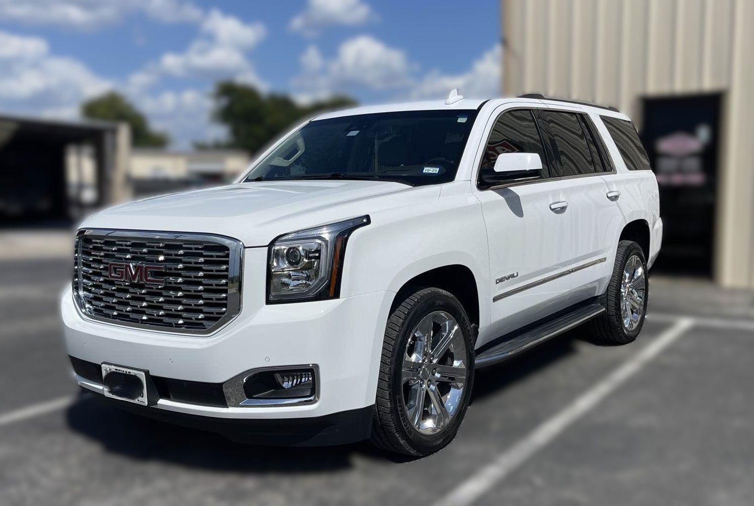 White GMC Yukon SUV parked in front of a building on a sunny day.